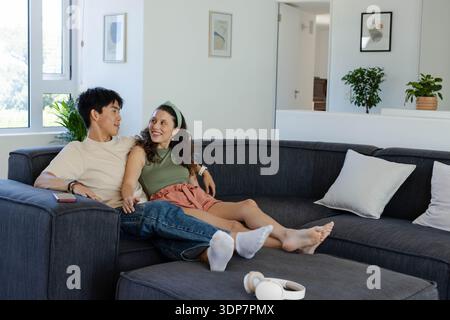 Verschiedene Paare sitzen dicht auf dunkelgrauem Sofa in hellem Wohnzimmer mit Smartphone Stockfoto