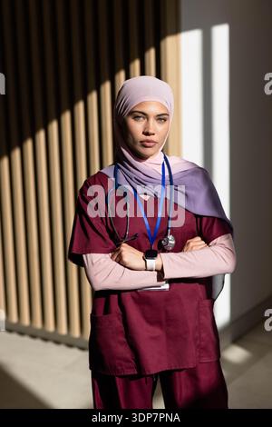 Afroamerikanische Krankenschwester stehende Arme in Klinik kastanienbraunen Peelings pastellfarbene Hijab Stethoskop Stockfoto