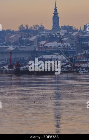 Schwere Baumaschinen und Kräne auf einem Binnenschiff standen im Winter im Kontrast zur historischen Architektur der Belgrader Altstadt. Stockfoto