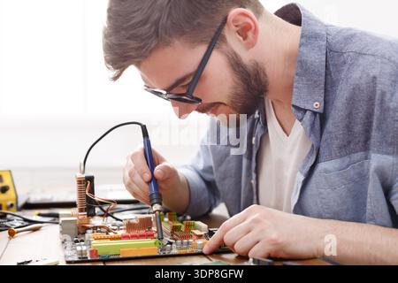 Man arbeitet an einer Leiterplatte mit einem Lötkolben in einem hellen Raum mit Werkzeugen Stockfoto