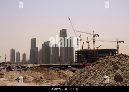 Große Haufen Schmutz und schwere Baukräne auf einer aktiven Baustelle, auf der moderne Wolkenkratzer im Stadtzentrum von Dubai entwickelt werden. Stockfoto