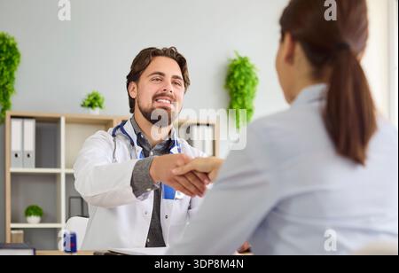 Handschlag glücklicher junger Ärztin und Patientin bei Sprechstunde im Krankenhaus Stockfoto