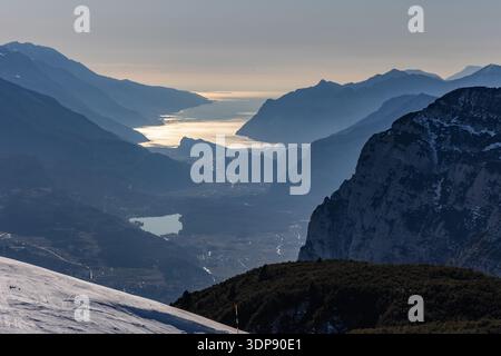 Goldenes Sonnenlicht reflektiert auf dem Gardasee zwischen Bergsilhouetten, Panorama-Alpenlandschaft in Norditalien. Stockfoto