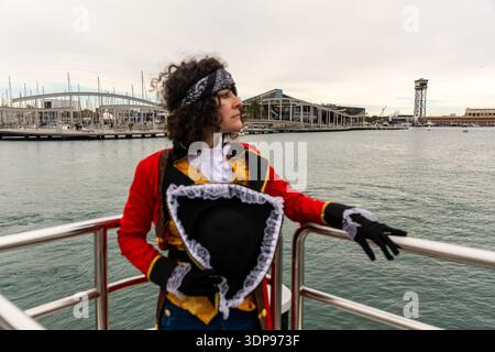 Frau in Piratenkostüm und Bandana, die auf einem Bootsgeländer steht. Einen Tricornhut halten und einen geschäftigen Hafen mit Segelmännern überblicken Stockfoto