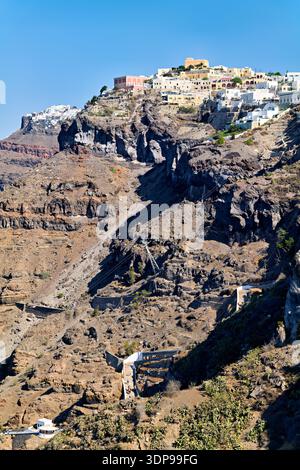 Touristen und Einheimische steigen die steilen Caldera-Klippen in Fira, Santorin, Griechenland auf/ab, mit der Seilbahn oder mit Eseln auf dem gewundenen Pfad. Stockfoto