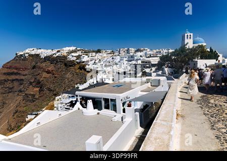 Touristen schlendern durch Oia, Santorin, Griechenland und bewundern die berühmten weißen Gebäude, die Kirche mit blauer Kuppel und den atemberaubenden Blick auf die Caldera. Stockfoto
