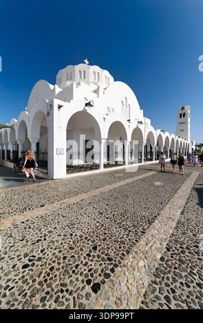 Touristen spazieren vorbei an der wunderschönen weißen Metropolitan Kathedrale von Thira in Fira, Santorin, Griechenland, und genießen den sonnigen Tag. Stockfoto