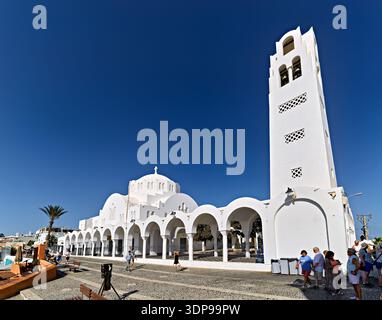 Touristen erkunden die wunderschöne weiße orthodoxe Metropolitan Kathedrale in Fira, Santorin, Griechenland, und genießen den sonnigen Tag und die berühmte Architektur. Stockfoto