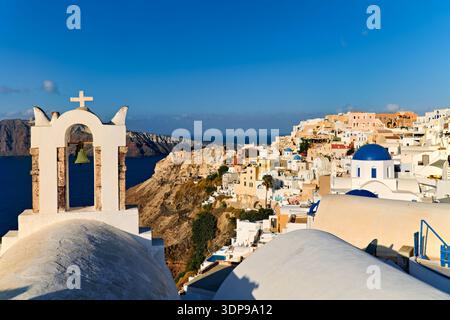 Santorin, Griechenland: Ein Glockenturm umrahmt die berühmte weiß-blaue Architektur des Dorfes Oia, der über der Caldera thront und Besucher weltweit anzieht Stockfoto