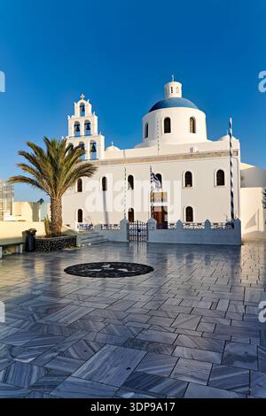 Berühmte weiße Kirche mit blauer Kuppel und Glockenturm in Oia, Santorin, Griechenland, ein atemberaubendes Beispiel traditioneller kykladischer Architektur. Stockfoto