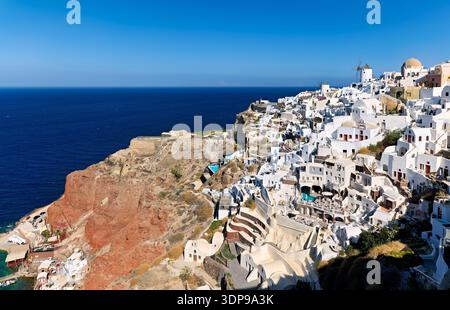Oia Village, Santorin, Griechenland, mit seinen berühmten weißen Gebäuden und Windmühlen auf den Caldera-Klippen mit Blick auf die tiefblaue Ägäis, ein po Stockfoto