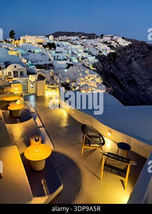 In Oia, Santorin, Griechenland, werden die berühmten weißen Gebäude und eine ruhige Außenterrasse beleuchtet, die perfekt zum Genießen der Caldera ist Stockfoto