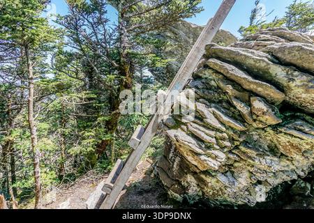 Eine hölzerne Leiter lehnt sich an einen großen Felsen. Der Felsen ist mit Moos bedeckt und hat eine raue Textur. Die Szene ist friedlich und ruhig Stockfoto