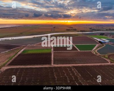 Blick aus der Vogelperspektive auf die Marktgartengrundstücke entlang eines Flusses unter dem farbenfrohen Sonnenuntergangshimmel in Werribee South in Victoria, Australien. Stockfoto