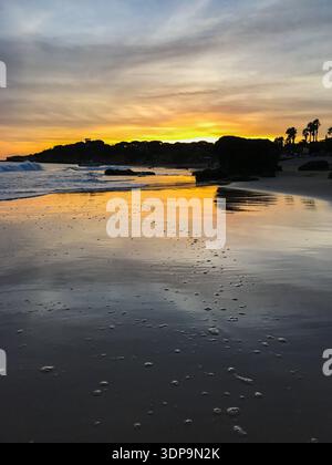 Landschaftsblick auf einen Strand in Portugal kurz nach Sonnenuntergang, in warmen Gold- und Gelbtönen getaucht. Das schwindende Licht des Himmels reflektiert über ruhiges Wasser. Stockfoto