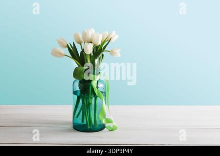 Frische weiße Tulpen in einer grünen Vase mit einem Band auf einem Holztisch Stockfoto