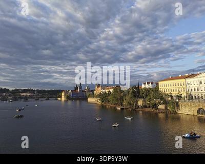 Prag in der Abendsonne. Moldau umgeben von beleuchteten historischen Gebäuden, kleinen Booten, die auf ruhigem Wasser schwimmen, Prag, Tschechische Republik Stockfoto