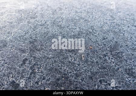 Nahaufnahme von Frostkristallen, die eine dunkle Oberfläche bedecken, wodurch eine natürliche Wintertextur und ein abstraktes Eismuster entstehen Stockfoto