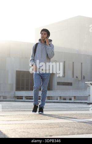 Afroamerikanischer Mann, der auf dem Dach läuft und Telefon an Ohr hält, Hoodie-Jeans mit Rucksack trägt Stockfoto