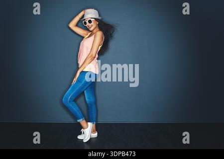 Mode, Platz und Frau mit Sonnenbrille im Studio mit kreativem, lässigem oder trendigem Outfit. Lächeln, Hut und Porträt einer Person mit Selbstvertrauen Stockfoto