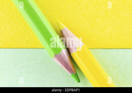 Gelbe und grüne Farbstifte auf gelb-grünen, diagonal angeordneten Hintergrundpapieren. Minimalistische Komposition Stockfoto