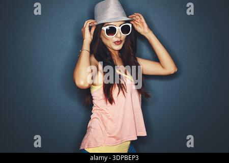Mode, Sonnenbrille und Frau im Studio, Fedora und stilvolle Kleidung auf dunklem Hintergrund. Sonnenschirme, trendy und Person mit Glück, Brillen und Stockfoto