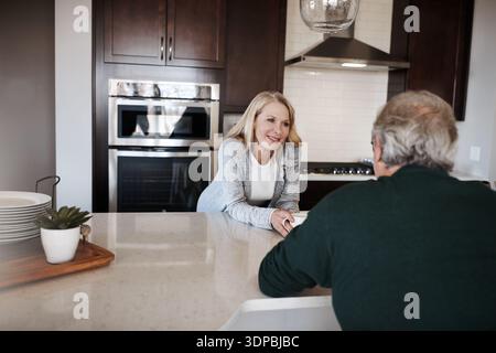 Seniorenpaar, Gespräch und Morgen in der Küche mit Kaffee für Gespräche oder Diskussionen zu Hause. Ältere Menschen, Mann und Frau, die mit einem Lächeln sprechen, Koffein Stockfoto