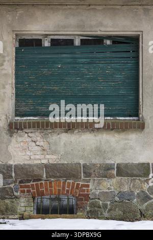 Kaputte türkisfarbene Fensterläden an einem verfallenen alten Haus im Winter in Europa Stockfoto