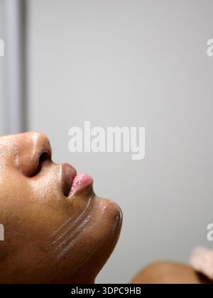 Afroamerikanisches Frauenprofil bei der Gesichtsreinigung. Minimalistischer Hintergrund mit negativem Platz für Marketingtexte oder Markentitel für Hautpflege. Stockfoto