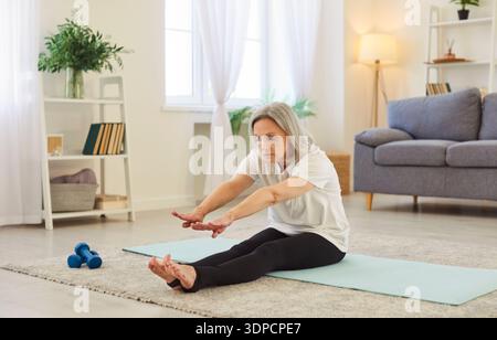 Yogi fit alte sportliche Seniorin, die Yoga zu Hause übt, sitzend, dehnend, entspannend posiert Stockfoto