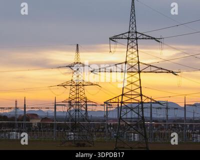 Die Schaltanlage der Hochspannungs-Umspannwerke zeigt Transformatoren und Übertragungsleitungen während des dramatischen Sonnenuntergangs in einem ländlichen Gebiet. Stockfoto