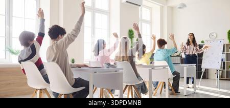 Teenager-Schüler heben die Hände, um Fragen im modernen Klassenzimmer mit dem Lehrer zu beantworten Stockfoto