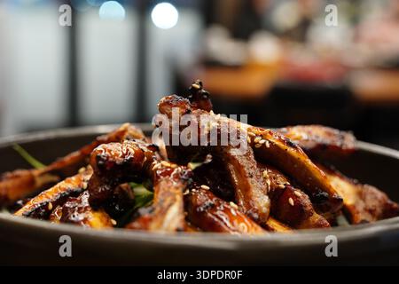 Köstliche koreanische gegrillte Schweinerippchen vom Grill, Jjokgalbi, mit Sesamsamen und grünen Zwiebeln auf einem schwarzen Teller Stockfoto