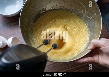 Draufsicht auf die Ei- und Zuckermischung, die mit einem elektrischen Mixer in einer Metallschale zu einem glatten Teig geschlagen wird. Stockfoto