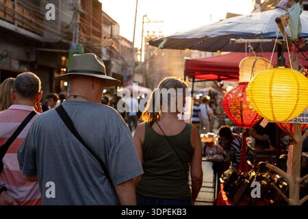 Ein Rückblick auf Touristen, die durch einen überfüllten Markt in Südostasien laufen. Das warme, goldene Licht des Sonnenuntergangs beleuchtet die Szene, Highlight Stockfoto