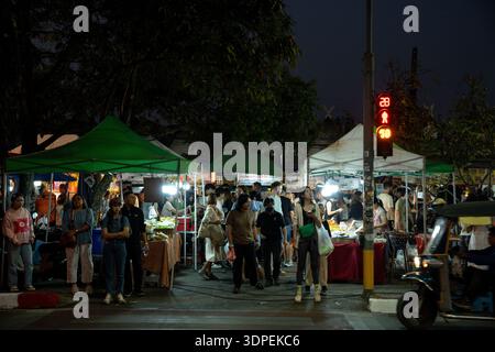 Eine geschäftige Menschenmenge von Einheimischen und Touristen erkundet abends einen lebhaften Street Food Markt in Chiang Mai, Thailand. Die Szene wird durch Standlicht beleuchtet Stockfoto