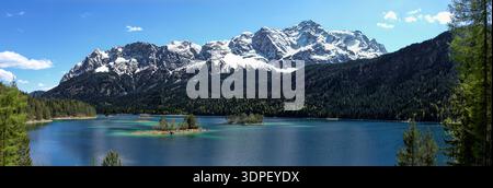 Das Foto fängt eine atemberaubende bayerische Alpenlandschaft mit dem kristallklaren Eibsee ein, der die Zugspitze unter einem hellblauen Himmel und warmen s reflektiert Stockfoto