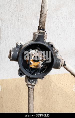 Nahaufnahme eines offenen elektrischen Anschlusskastens mit freiliegender Kupferverkabelung an einer Wand, die beschädigte Isolierung und industrielle elektrische Komponenten zeigt Stockfoto