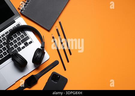 Kopfhörer, Laptop, Smartphone, Smart Watch und Schreibwaren auf orangefarbenem Hintergrund, flach gelegt. Leerzeichen für Text Stockfoto