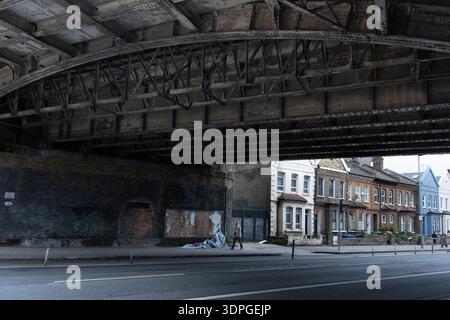 Unter der Eisenbahnbrücke an der Queenstown Road Station Battersea laufen die Menschen vorbei an viktorianischen Reihenhäusern. Stockfoto