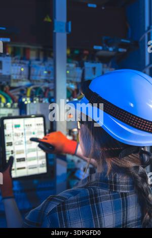Elektrikerin verwendet Tablettenschemata in der Nähe von Schaltschränken. Nahaufnahme-Steuerung. Stockfoto