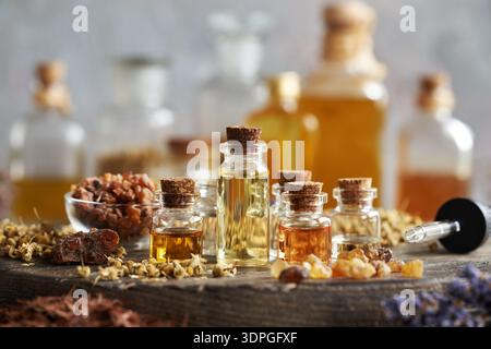 Auswahl ätherischer Öle in Glasflaschen mit Weihrauch, Myrrhe, Lavendel und anderen getrockneten Kräutern und Blüten Stockfoto