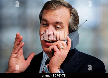 Der Mann spricht und benutzt ihn einfach mit den Händen, mit Spannung auf einem alten Handy, während er tagsüber einen fröhlichen Ausdruck in einer offenen Tür-Umgebung zeigt Stockfoto