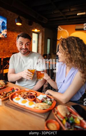 Ein paar Toasten mit Biergläsern während eines Mittagessens in einem Restaurant Stockfoto