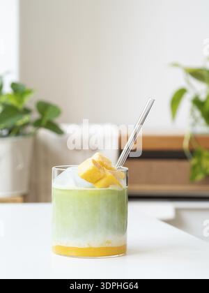 Eismatcha Latte mit tropischer Mango, Milch und klarem Stroh in einem Glas Stockfoto