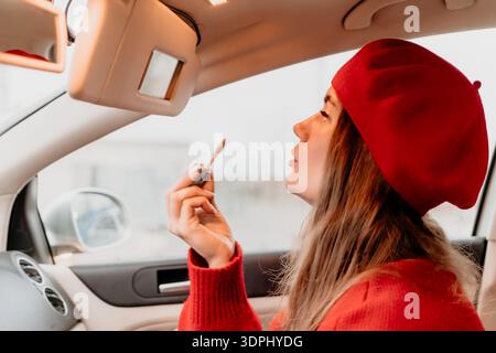 Make-up-Auto für Frauen. Die junge Frau trägt Lippenglanz im Auto mit einem Kosmetikspiegel auf. Stockfoto