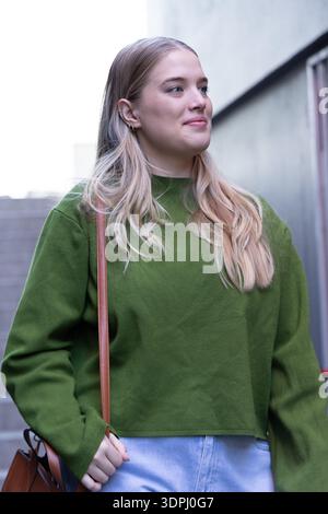 Frau aus den 20er Jahren, die im Treppenhaus an der Betonwand stand, in grünem Pullover und Jeans, mit braunem Riemen Stockfoto