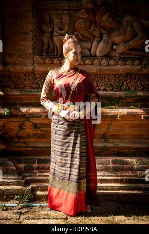 Eine wunderschöne Frau in traditioneller thailändischer Kleidung steht im dramatischen Sonnenlicht im Terracotta Garden Café in Lamphun, Thailand. Stockfoto