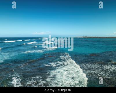 Tropische Strandlandschaft Meereswellen Rollen an einem sonnigen Karibiktag in Richtung einer ruhigen Küste unter klarem Himmel Stockfoto