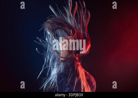 Schöne Frau, die Haare wirft, dynamisches Haar Flip Girl Porträt unter roter und blauer Neonbeleuchtung im Studio Stockfoto